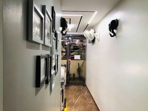 A narrow corridor hung with a column of black-framed prints, lit by a recessed ceiling strip, brown marble underfoot.