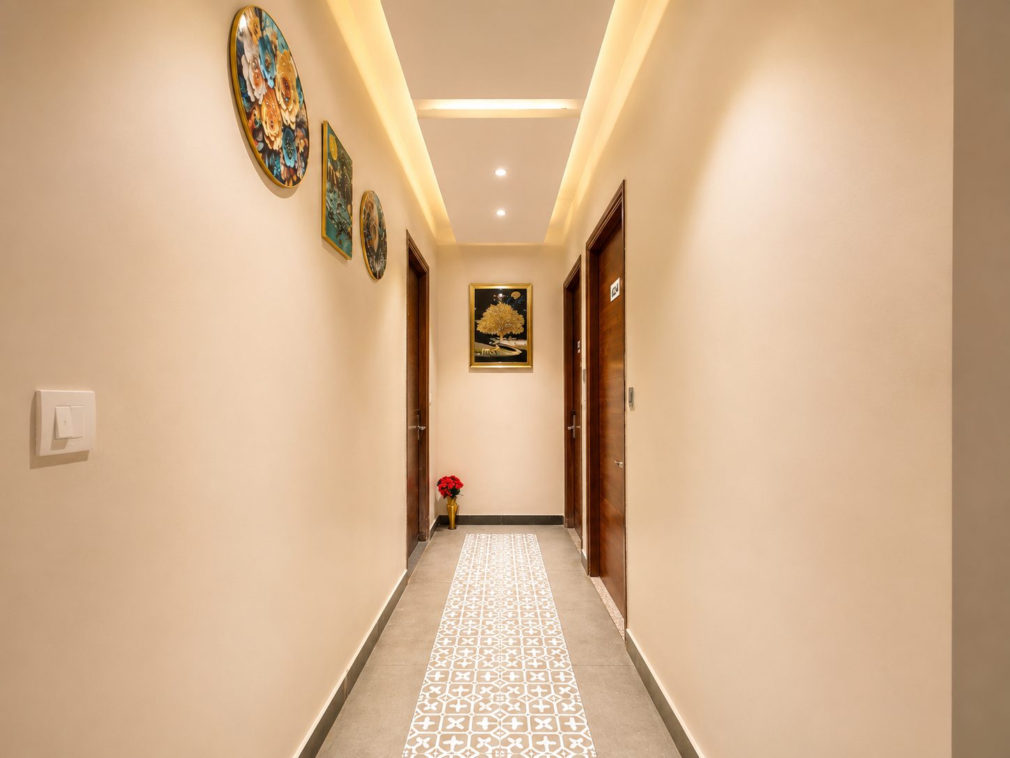 A guest corridor with a patterned tile runner down the middle, round decorative plates on the wall and a framed golden tree at the far end.