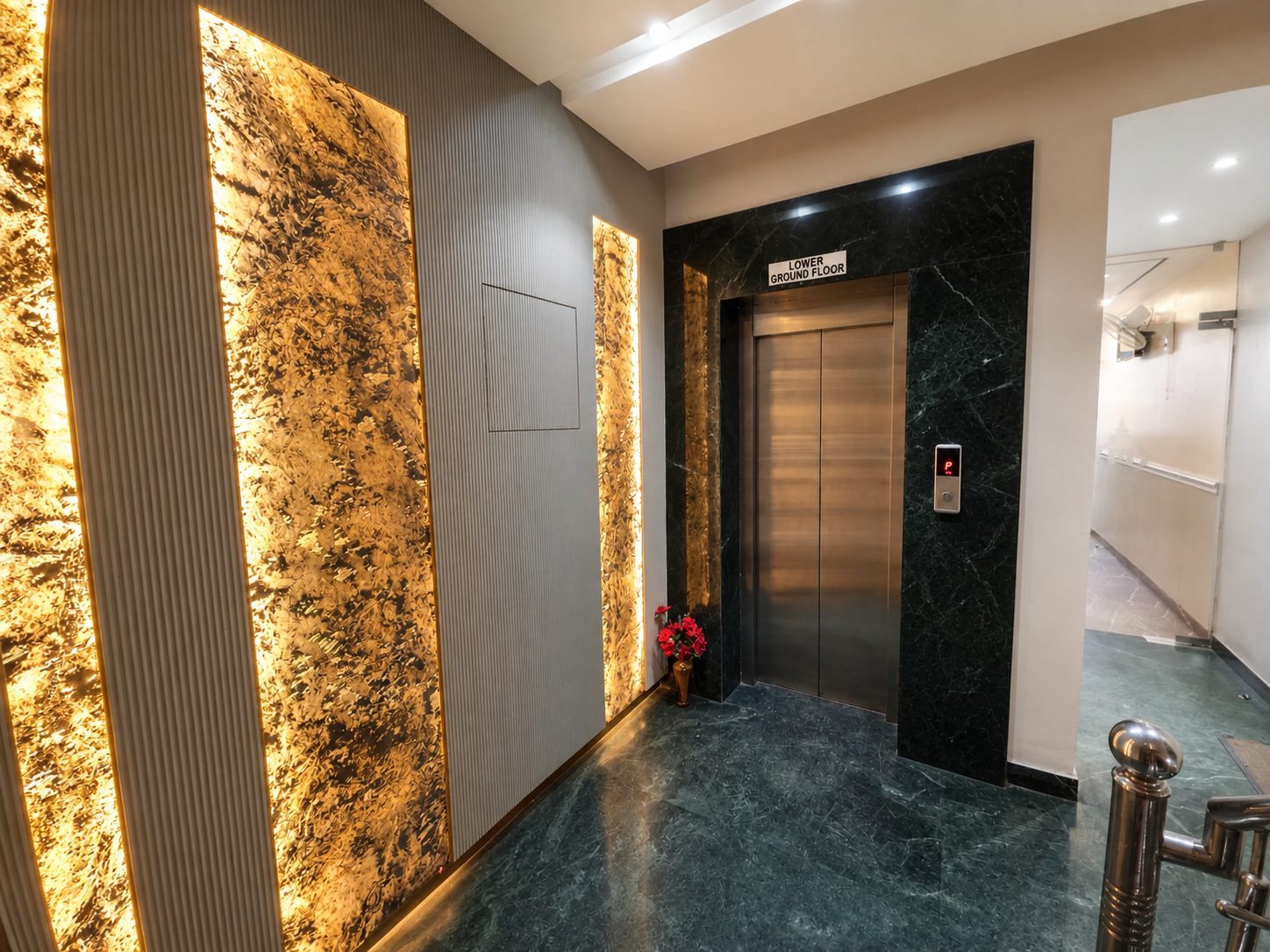 The lift lobby: steel lift doors framed in green marble, backlit amber stone panels on the wall and a green marble floor.