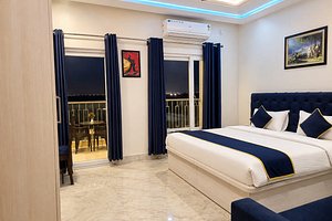 A Premier room with a navy upholstered headboard, white bedding and a curtained balcony doorway leading to a small seating area.