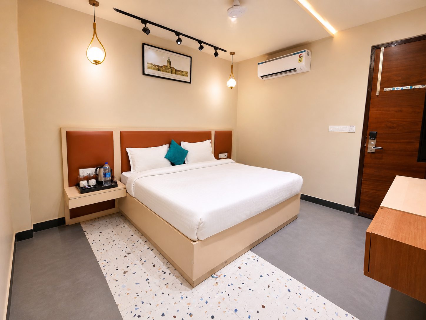 A guest room with a king bed under a rust-orange upholstered headboard, two brass pendant lamps, a framed sketch above the bed and a speckled terrazzo floor strip.
