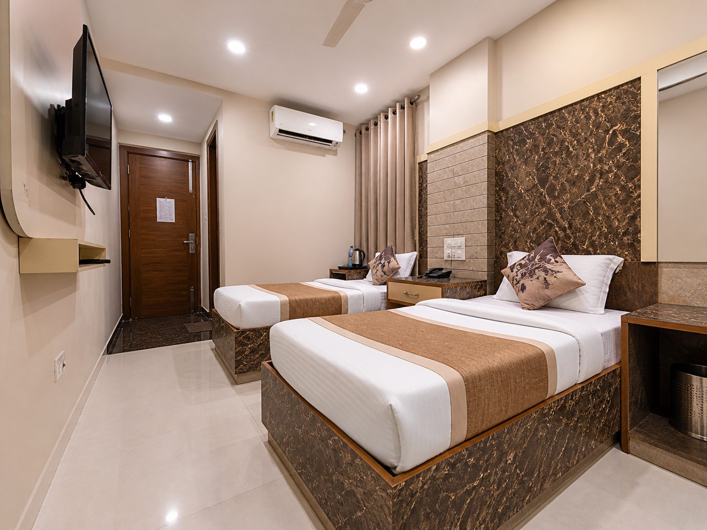 A twin room with two single beds against a brown marble-pattern wall, a telephone on the table between them and the door at the end of the room.