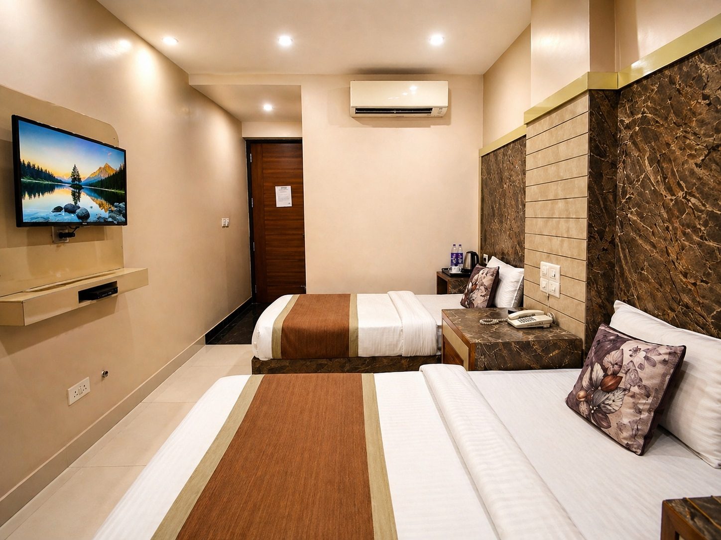 The Twin room seen from the window end: two single beds side by side, a wall-mounted television opposite and the door at the far end.